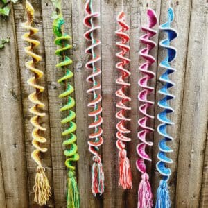 Wind Spinners made by Sarah Lou Crafts in five different designs of and colours show hanging from a green garden bush as ornaments and can also be used as window hangings.