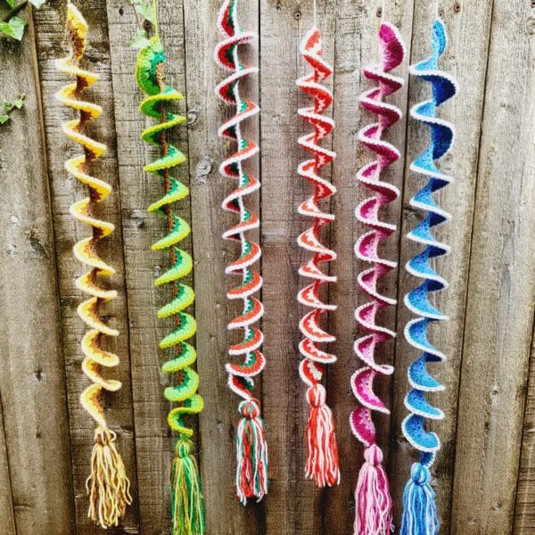 Wind Spinners made by Sarah Lou Crafts in five different designs of and colours show hanging from a green garden bush as ornaments and can also be used as window hangings.