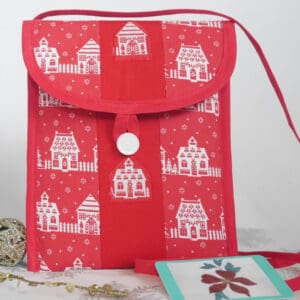 Small patchwork bag made from red and white cotton fabrics showing houses in snow, with red trim and narrow strap, white button closure