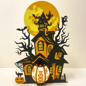 A 28cm haunted house lantern made from cardstock and parchment paper. The lantern features a spooky house, a pumpkin lantern with jack-o'-lantern faces, bats, ghosts, and fairy lights.