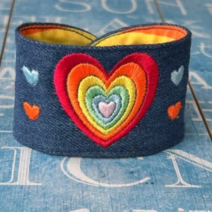 Rainbow colours with a big heart and small hearts embroidered on blue denim displayed against a blue background