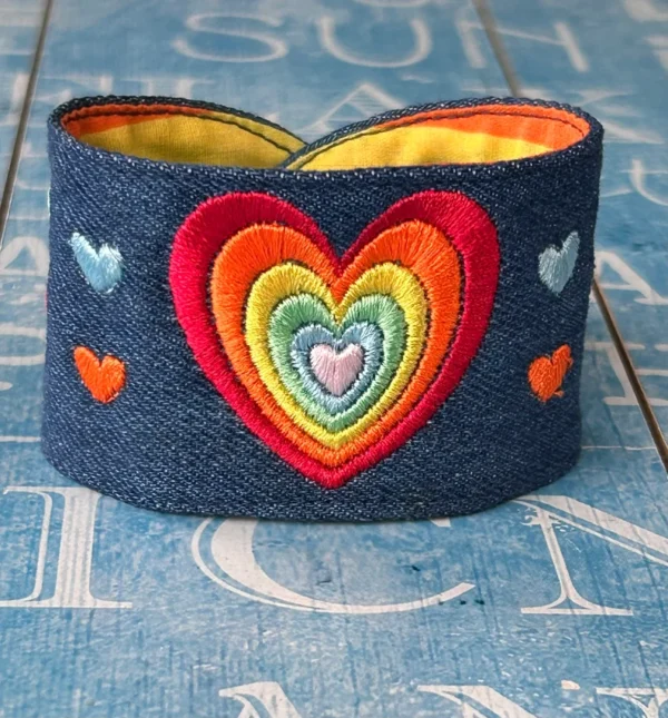 Rainbow colours with a big heart and small hearts embroidered on blue denim displayed against a blue background