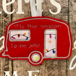 Red felt caravan hanging against a brown background. Words say ,‘it’s the season to be jolly