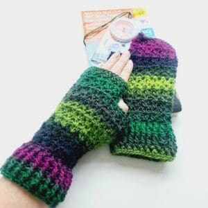 Multicoloured crochet fingerless mitts by Sarah Lou Crafts in a variegated colourway of purple and green stripes. Shown modelled on makers hand laying on top of a map and compass as props.