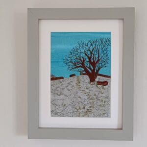 Fabric picture of oak tree in winter on snowy hillside with embroidered detail, framed with white mount and in grey frame.