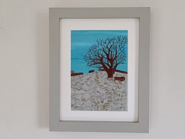 Fabric picture of oak tree in winter on snowy hillside with embroidered detail, framed with white mount and in grey frame.