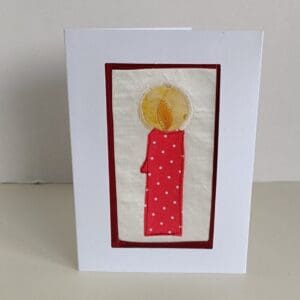 Greetings card showing a textile red spotted candle with yellow halo around flame, set on a shiny fabric background and in a white mount