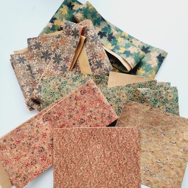 Cork Fabric off cut pieces by Sarah Lou Crafts shown on a white table in a bundle of patterns including, green leaves, flower print, green or pink floral, pink blossom and rainbow fleck.