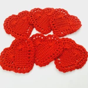 Crochet red heart mug rug coaster mats set of 6 by Sarah Lou Crafts arranged in a fan of two rows of three on a white table.