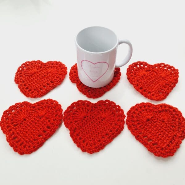 Set of 6 red crochet heart drinks coasters arranged in two rows of three with a white mug shown on the top middle mat by Sarah Lou Crafts.