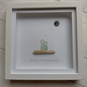 'Love You To The Moon and Back' is a picture handmade using a mix of seaglass and driftwood, in shades of seafoam and whites, collected from Cornwall with the addition of a navy and gold button.