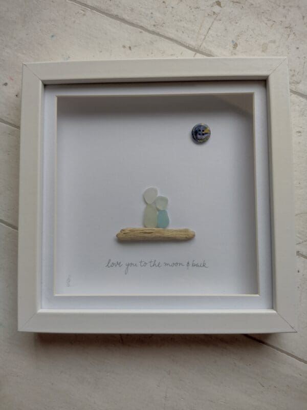 'Love You To The Moon and Back' is a picture handmade using a mix of seaglass and driftwood, in shades of seafoam and whites, collected from Cornwall with the addition of a navy and gold button.