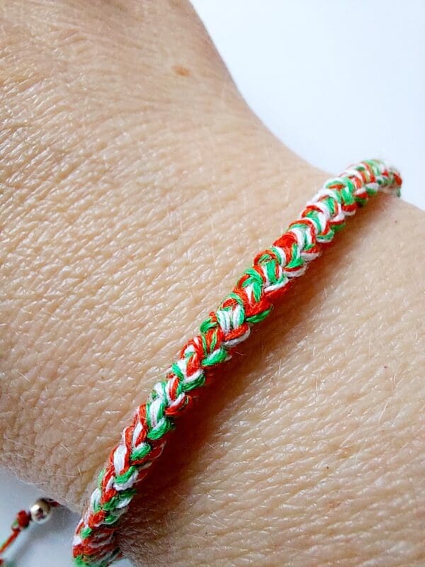 Close up image of Crochet cord bracelet using red, white and green cotton thread on model's wrist to show the colours and braided pattern of the product by Sarah Lou Crafts.