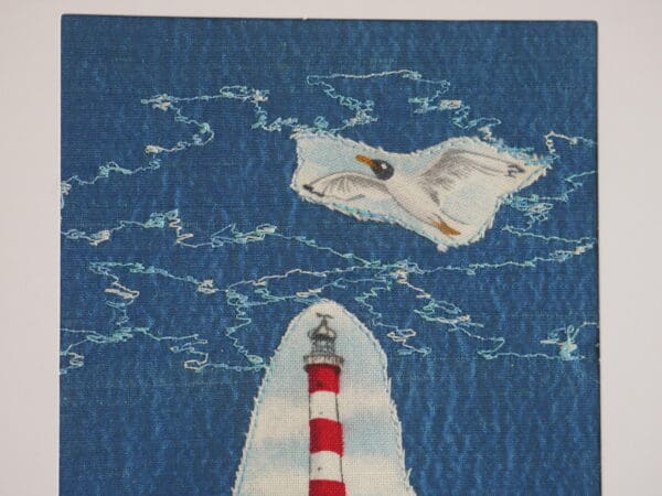 Detail of part of textile collage showing top of lighthouse, sea gull and freehand machine stitching on blue silk background.