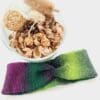 Rocket crochet ear warmer headband made by Sarah Lou Crafts in a purple and green variegated yarn, shown laying flat on a white table with a bowl of pot pourri to the side.