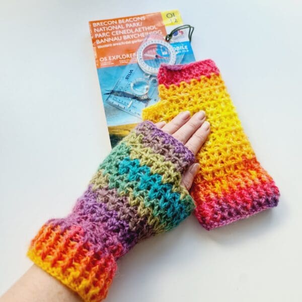 Rainbow crochet gloves, made by Sarah Lou Crafts. Shown being worn with a map and compass above.