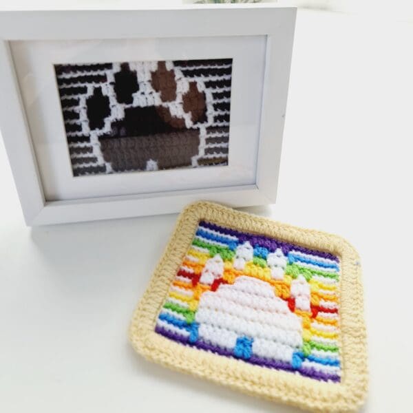 Paw print picture and mat made by Sarah Lou Crafts, Framed picture in brown and white to represent a chocolate Labrador dog. Shown in a white box frame with unframed rainbow paw print mat laying next to it both on a white table.