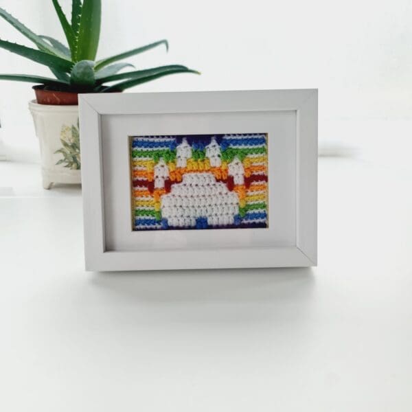 Framed picture of a dog's paw print in white with a rainbow stripe background, shown in a white box frame.