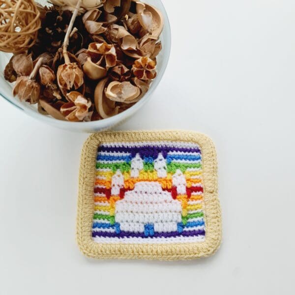 White Paw Print mat with a rainbow background and cream border made by Sarah Lou Crafts, shown laying flat on a white table.