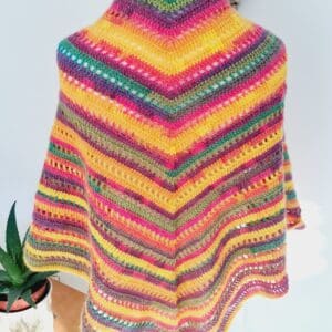 Triangle crochet shawl wrap by Sarah Lou Crafts in a variegated rainbow yarn made in colourful stripes. Shown on a white dress makers mannequin with a back view.