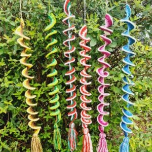 Wind Spinners made by Sarah Lou Crafts in five different designs of and colours show hanging from a green garden bush as ornaments and can also be used as window hangings.