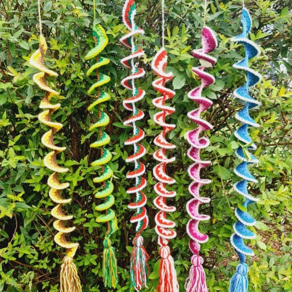 Wind Spinners made by Sarah Lou Crafts in five different designs of and colours show hanging from a green garden bush as ornaments and can also be used as window hangings.