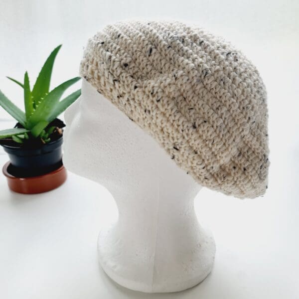 Side view image of a cream crochet beret. The circular shape is clearly visible, with the crown gathered at the top. The brim is defined and consistent.