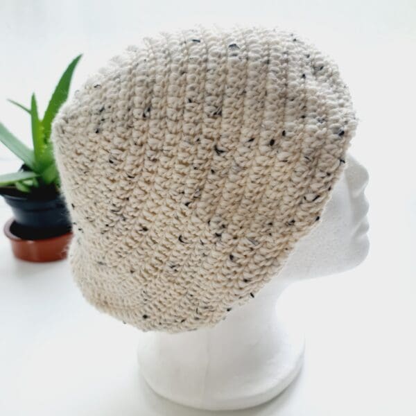 Close-up of a cream-colored crochet beret. The intricate stitch pattern creates a raised, textured surface. The yarn is soft and appears thick, ideal for winter warmth.