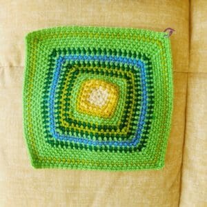 Crochet square using a moss stitch pattern with different coloured rows in greens and yellows to represent each day's top temperature for April 2025.