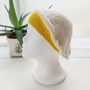 Side view of the cream and yellow cotton crochet beret hat by Sarah Lou crafts, emphasizing the gathered crown at the top. The hat's slouchy, relaxed shape is apparent.