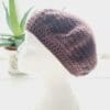Close-up of a dark grape coloured crochet beret. The intricate stitch pattern creates a raised, textured surface. The yarn is soft and appears thick, ideal for all year round style.
