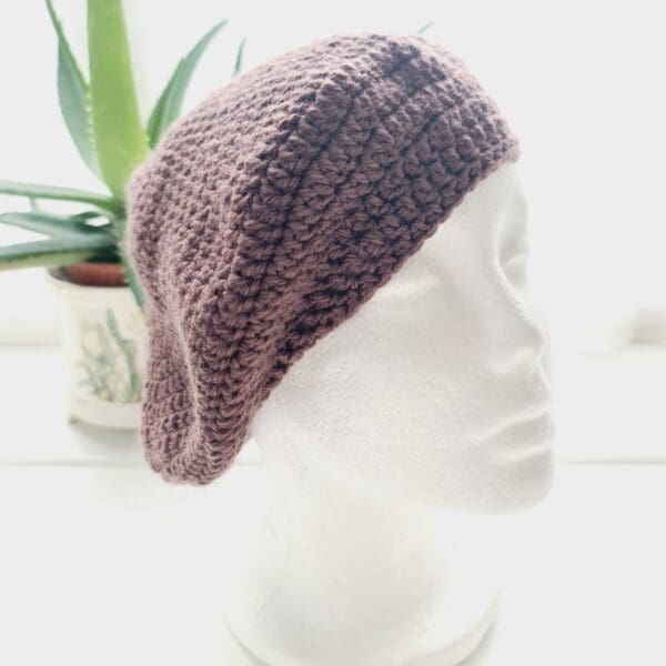 Crochet beret made by Sarah Lou Crafts using an aran yarn called Grape. Shown on white mannequin head with plant in back ground.