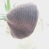 Side view image of a grape coloured crochet beret hat. The circular shape is clearly visible, with the crown gathered at the top. The brim is defined and consistent.