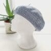 Close-up of a grey coloured crochet beret. The intricate stitch pattern creates a raised, textured surface. The yarn is soft and appears thick, ideal for all year round style.