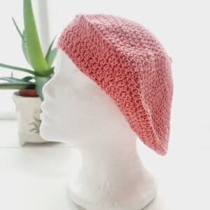 Side view of the pink cotton crochet beret hat by Sarah Lou crafts, emphasizing the gathered crown at the top. The hat's slouchy, relaxed shape is apparent.