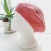 Close-up of a pink coloured crochet beret. The intricate stitch pattern creates a raised, textured surface. The yarn is soft and appears thick, ideal for all year round style.