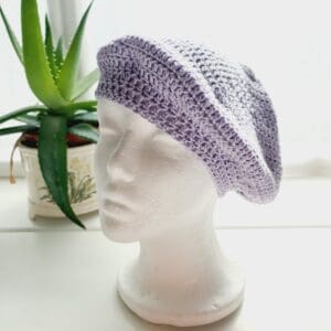 Close-up of a lilac purple coloured crochet beret. The intricate stitch pattern creates a raised, textured surface. The DK yarn is soft and lightweight, so ideal for spring and summer adventures.