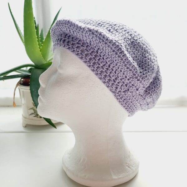 Side view of the pastel purple coloured crochet beret hat by Sarah Lou crafts, emphasizing the hat's slouchy, relaxed shape is apparent.