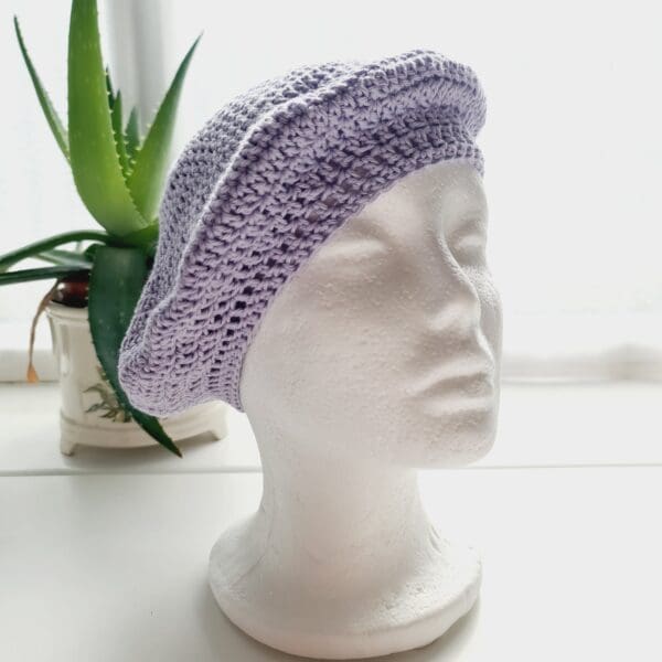 Crochet beret made by Sarah Lou Crafts using a pastel lilac cotton yarn. Shown on white mannequin head with plant in back ground.