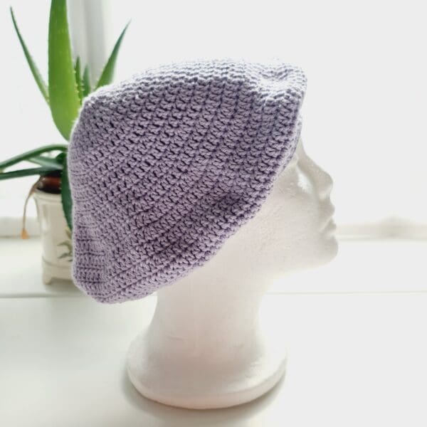 Side view image of a purple cotton crochet beret hat. The circular shape is clearly visible, with the crown gathered at the top. The brim is defined and consistent.