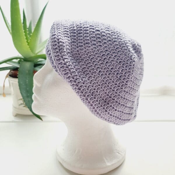 Side view of the lilac crochet beret hat by Sarah Lou crafts, emphasizing the gathered crown at the top. The hat's slouchy, relaxed shape is apparent.