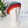 Detailed view of the bright rainbow crochet beret. The edge shows a neat, finished crochet stitch, highlighting the craftsmanship from Sarah Lou Crafts. The texture of the yarn is prominent.