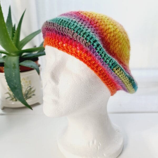 Close-up of a rainbow coloured crochet beret. The intricate stitch pattern creates a raised, textured surface. The DK yarn is soft and lightweight, so ideal for spring and summer adventures.