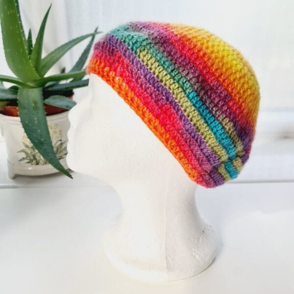 Close-up of a brightly coloured rainbow crochet beret. The intricate stitch pattern creates a raised, textured surface. The yarn is soft and lightweight, ideal for all year round style.