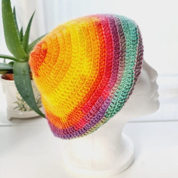 Side view image of a rainbow crochet beret hat. The circular shape is clearly visible, with the crown gathered at the top. The brim is defined and consistent.