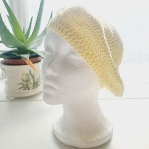 Close-up of a yellow coloured crochet beret. The intricate stitch pattern creates a raised, textured surface. The cotton yarn is soft and lightweight, so ideal for spring and summer adventures.