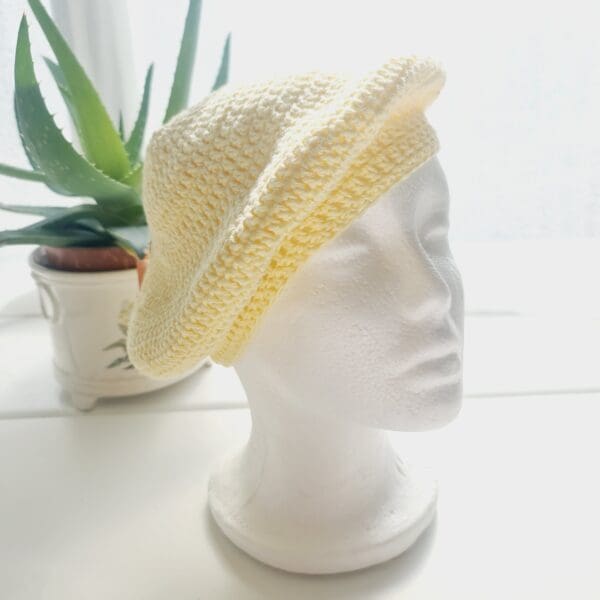 Crochet beret made by Sarah Lou Crafts using a pastel yellow cotton yarn. Shown on white mannequin head with plant in back ground.