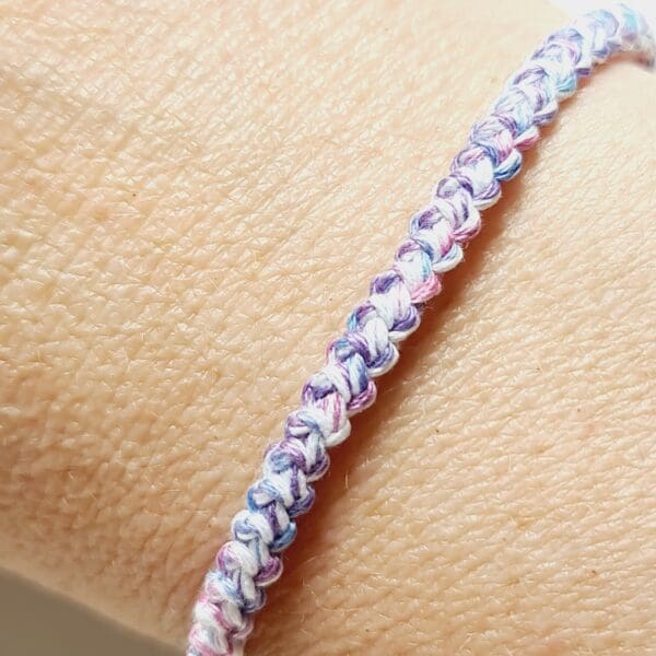 Close up image of Crochet cord bracelet using blue, pink, and white cotton threads on model's wrist to show the colours and braided pattern of the product by Sarah Lou Crafts.