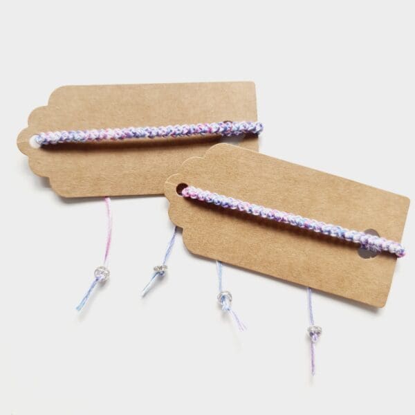 Trans pride friendship bracelets shown on brown gift tags made by Sarah Lou Crafts.