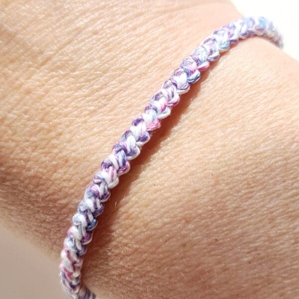 Crochet cotton cord bracelet by Sarah Lou Crafts in Trans flag colours of blues, pinks and white twisted threads. Shown modelled on makers wrist.